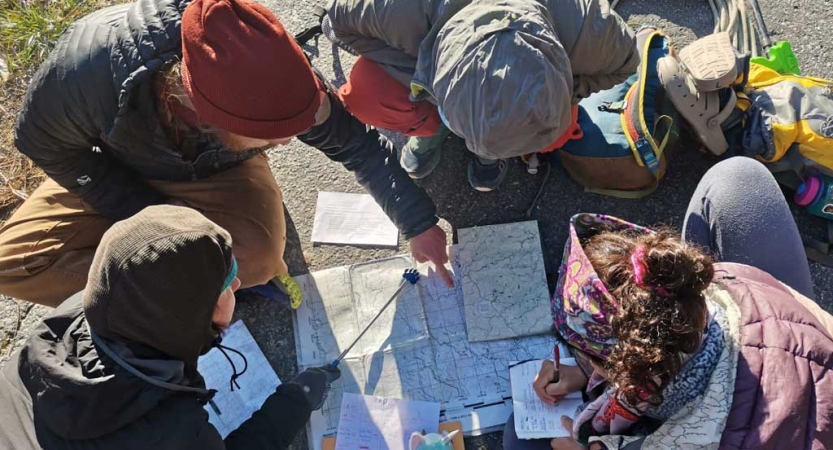 Four people examine a map that is spread out on the ground. 